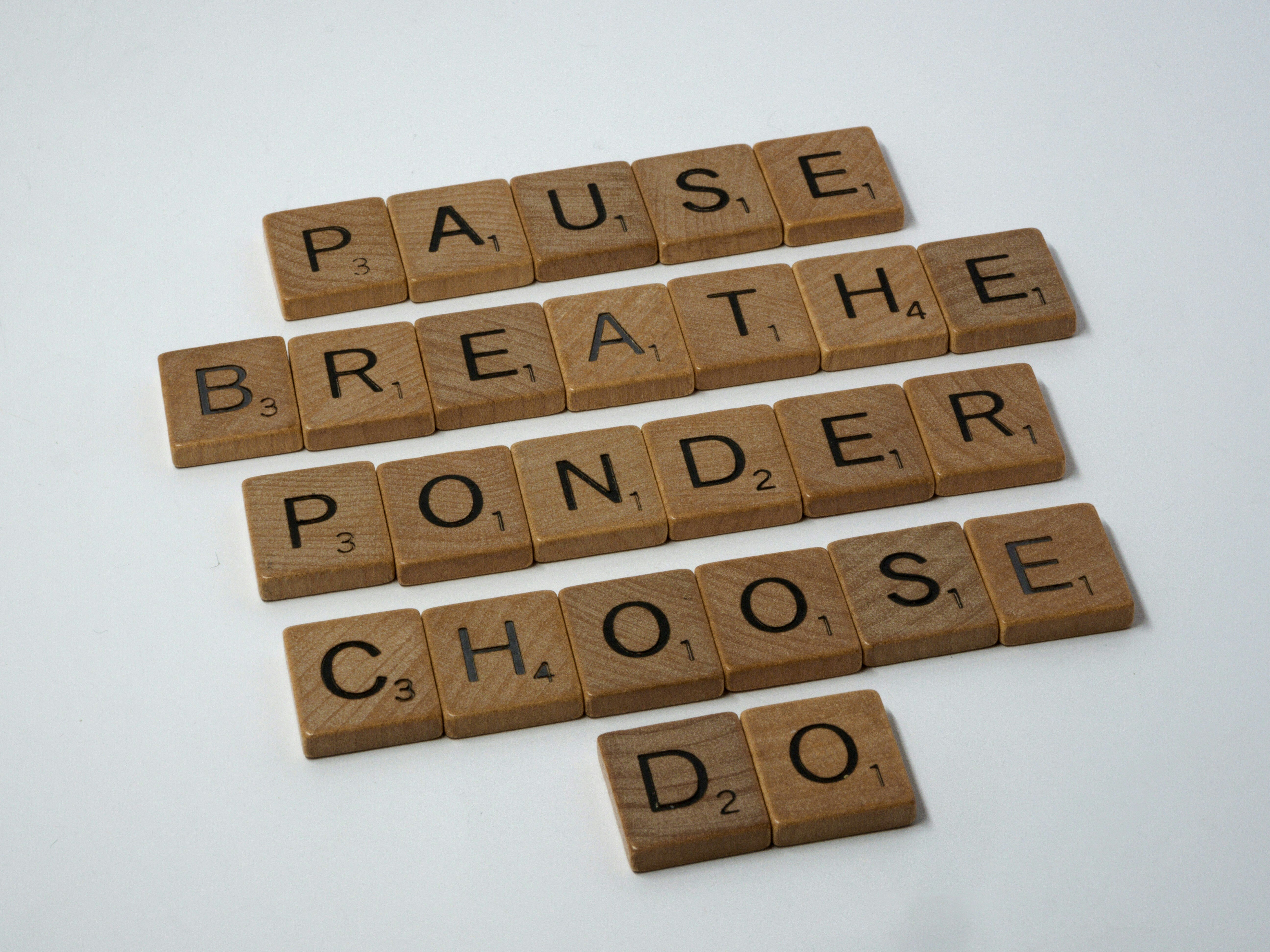 Brown wood scrabble tiles that spell out Pause Breathe Ponder Choose Do from top to bottom